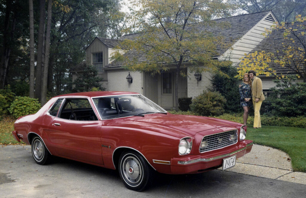 a couple next to a red 1974 ford mustang hardtop model