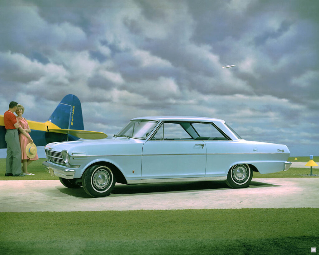 man and woman standing next to sky blue 1962 Chevrolet Chevy II Nova Sport Coupe