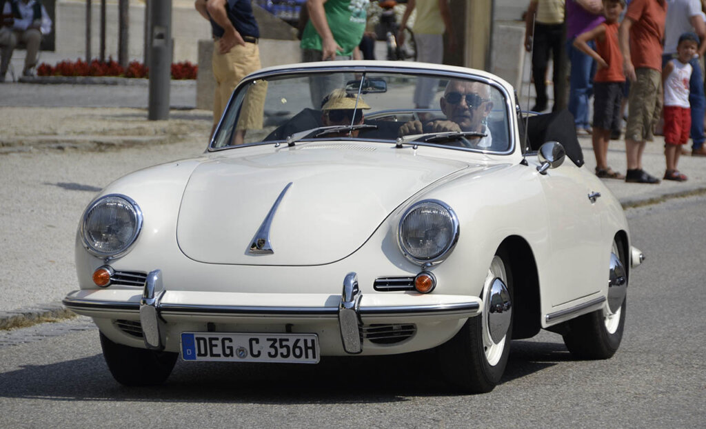 elderly couple driving in cream white porsche 356 C