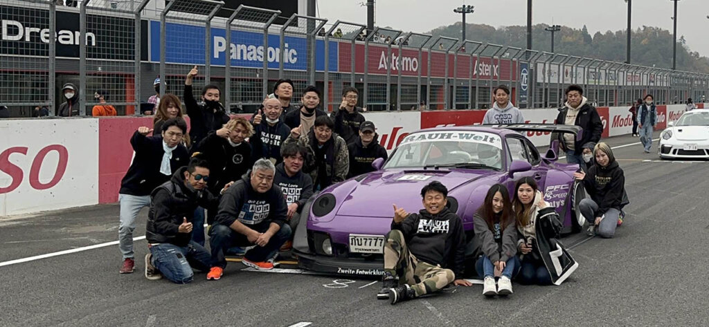 group of rwb members next to a purple porsche on a racetrack