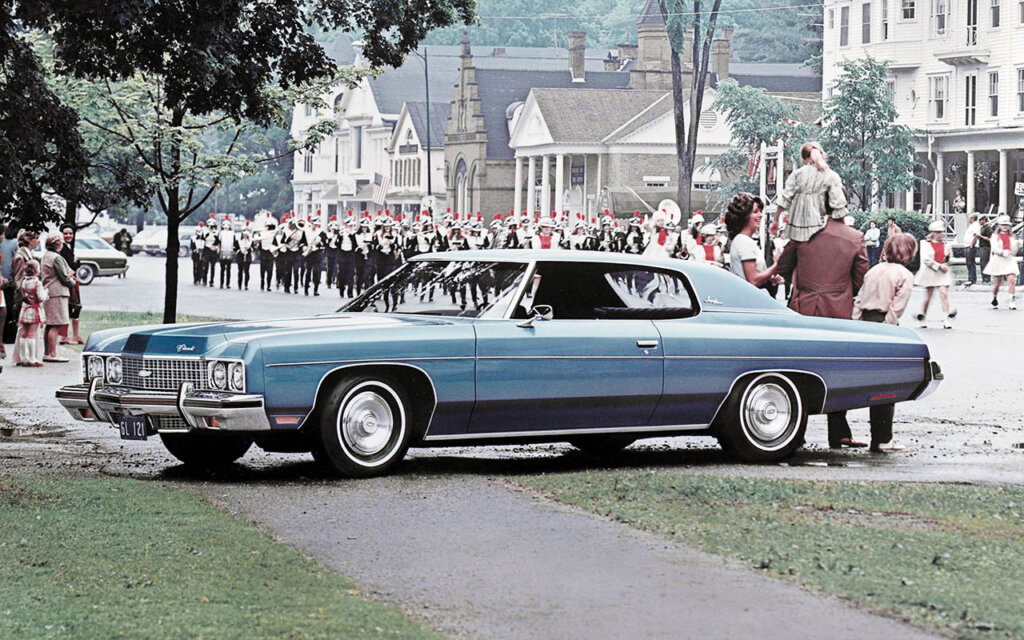 blue 1973 Chevrolet Impala Custom Coupe in a busy city street