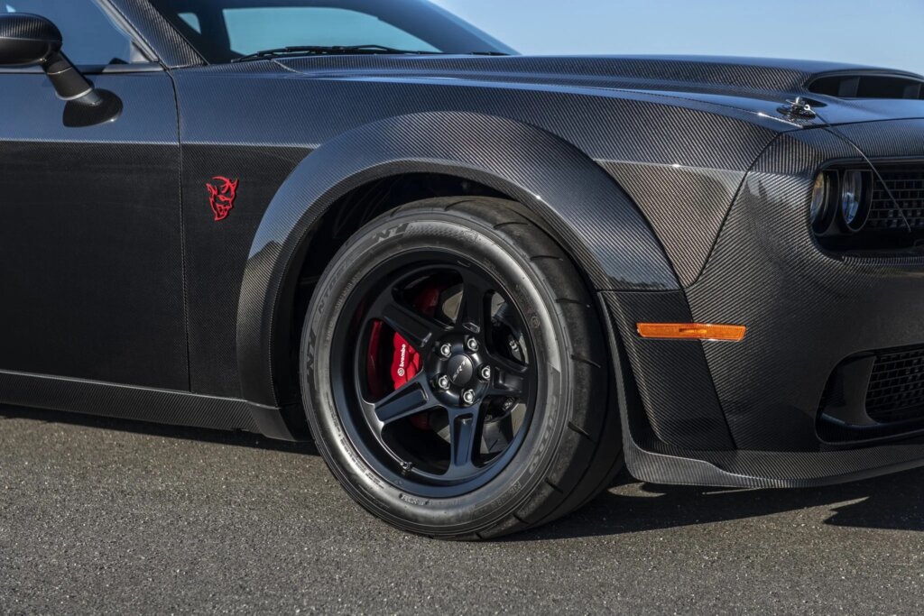Carbon Fiber Dodge Demon in the sunlight, front wheel and fender showing with red demon badge logo