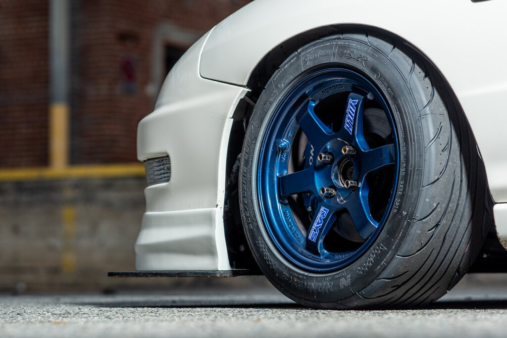 Blue Forged TE37s on a White Acura Integra, brick wall behind it