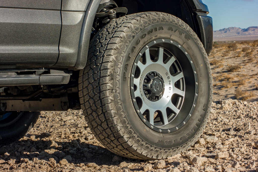 Silver wheel in the center and dark grey truck is parked on rocky road