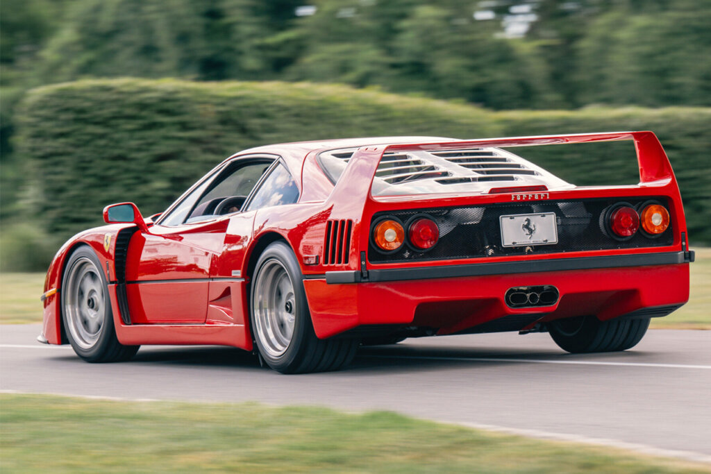 Rear side of the red Ferrari driving with grass on either side of it