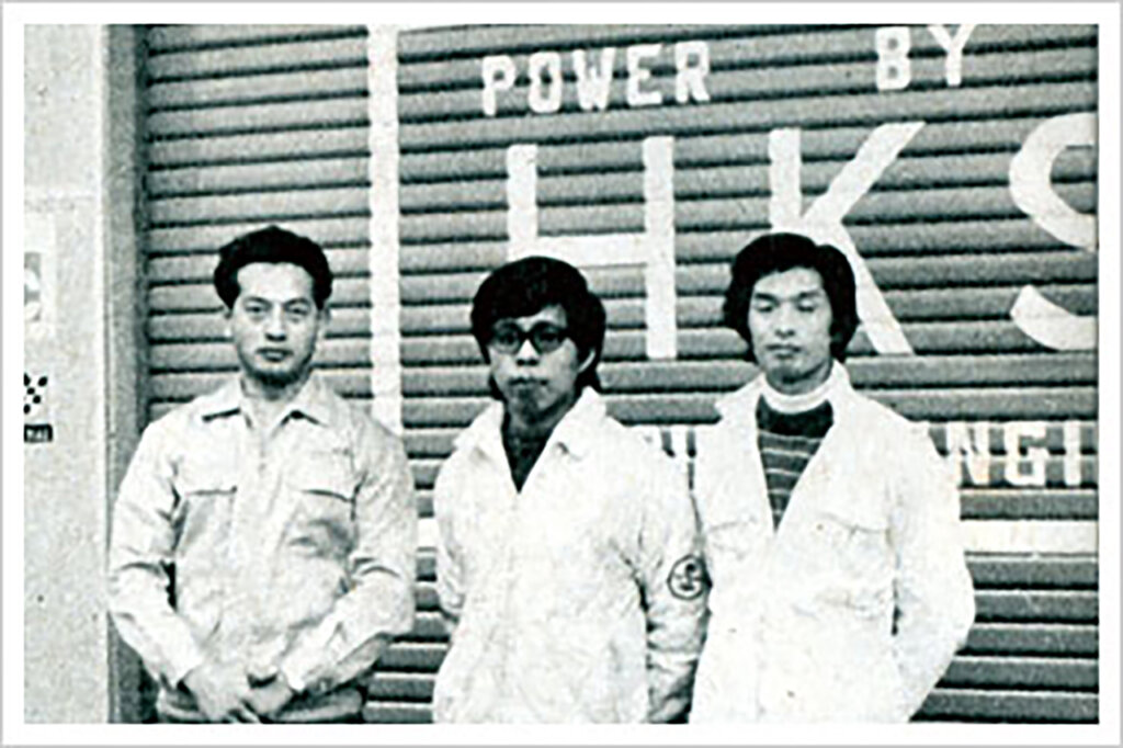 Three men infront of a garage that says HKS in white