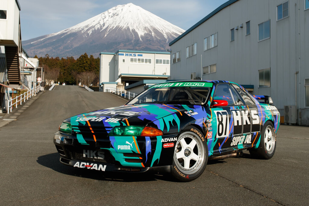 Nissan Skyline R32 with racing livery in front of the HQ building with Mt. Fuji behind it