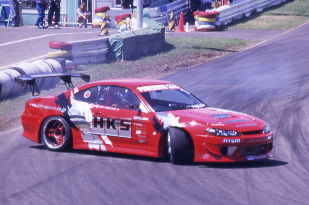 Red Nissan Silvia s15 drifting through a turn on a racetrack