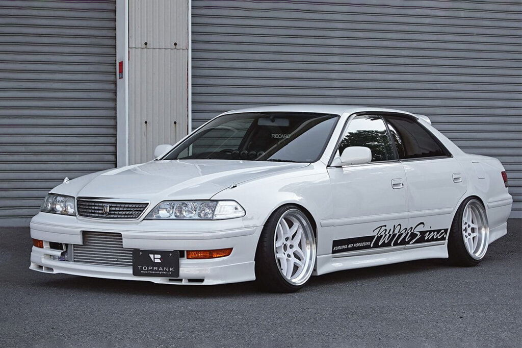 White Mark 2 in front of grey roll up garage doors on asphalt