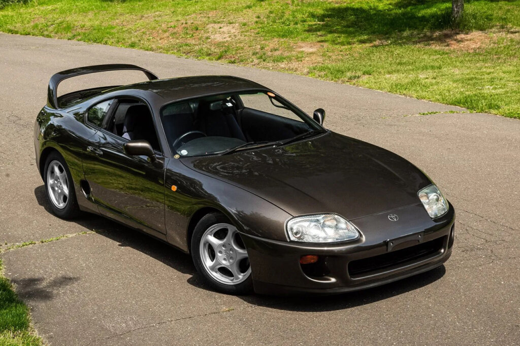 Dark brown MK4 Supra surrounded by grassy area and on concrete