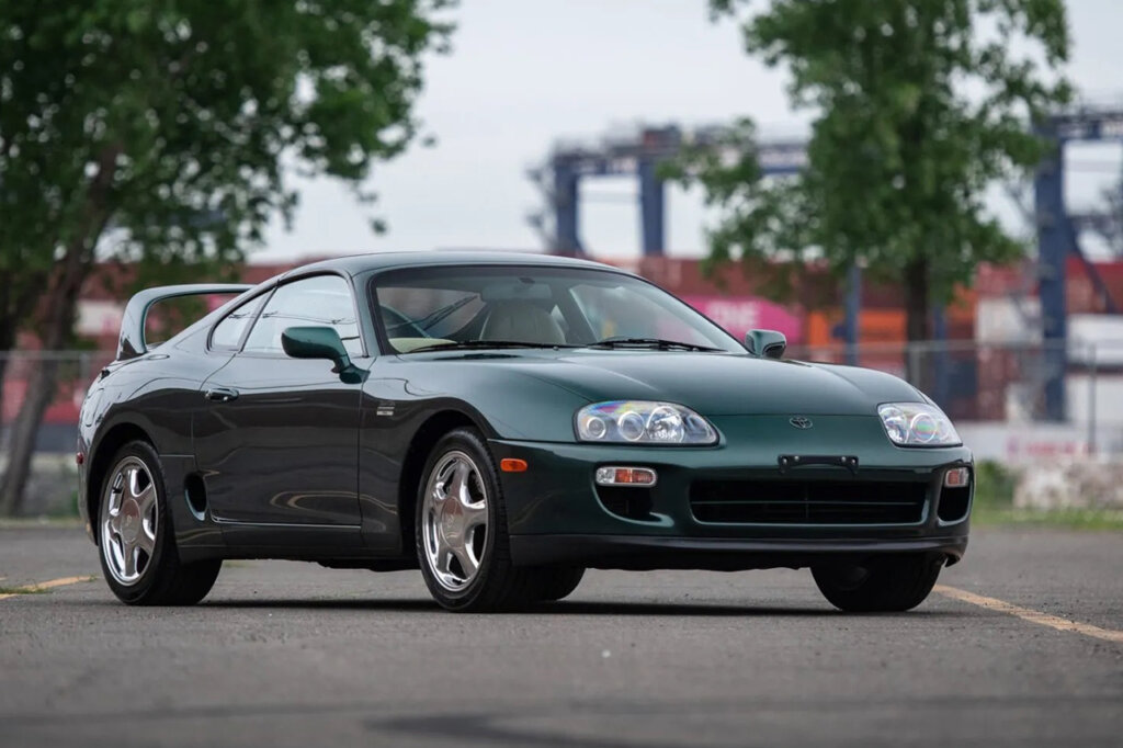 green MK4 Supra with trees in the background and car parked diagonally on ground