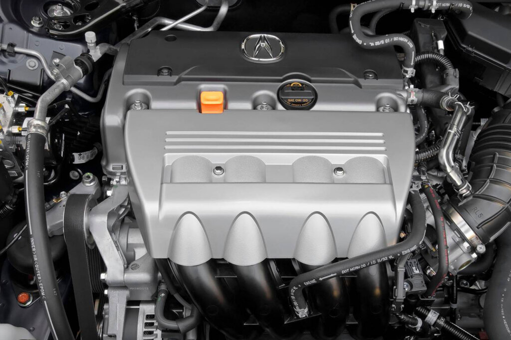 closeup of an engine, grey manifold cover with Acura logo