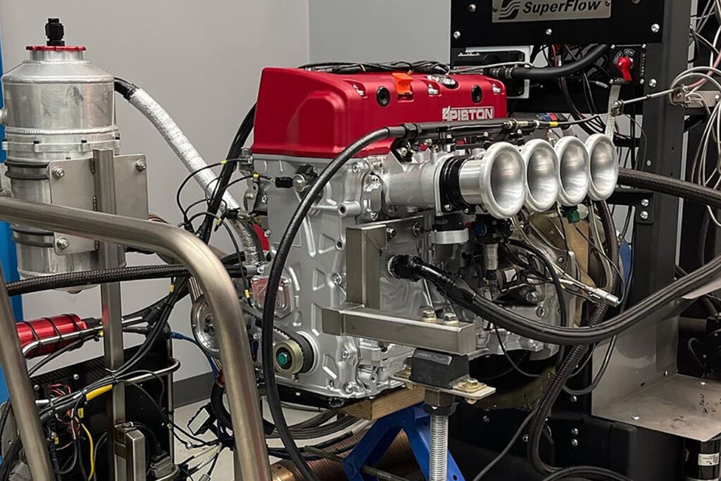 K20 engine with red cover and large openings on an engine stand with cables and tubing everywhere