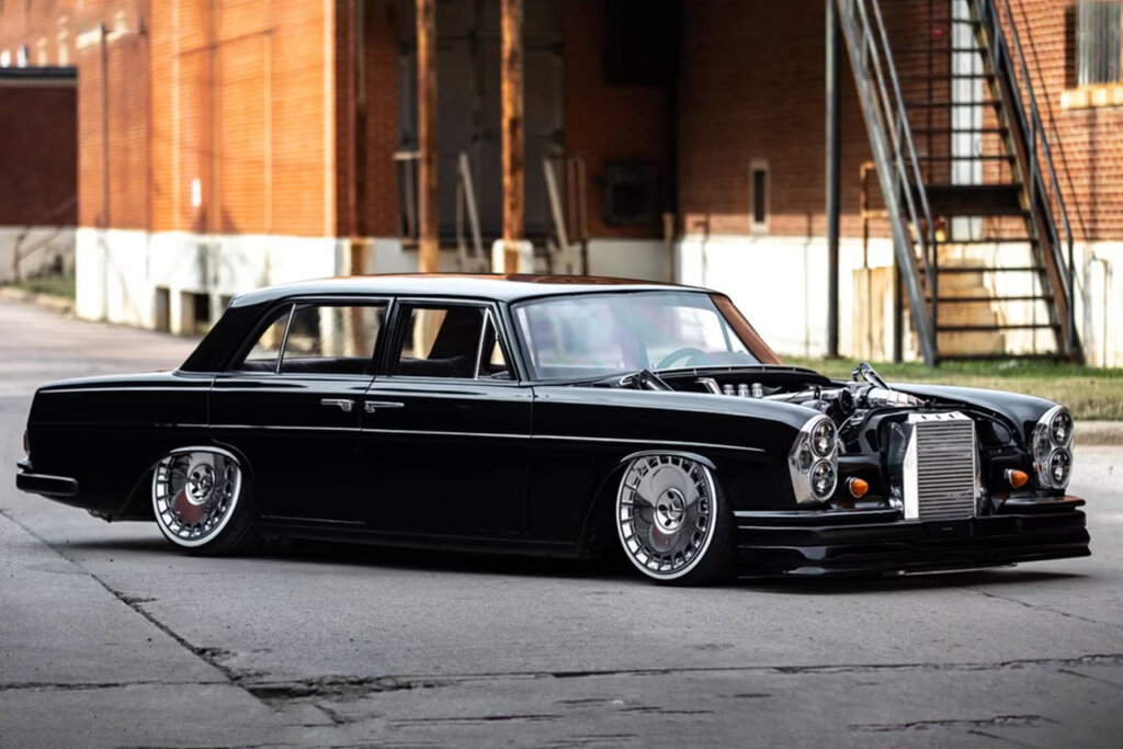 black 69' Mercedes in front of a brick building and parked on gray concrete that has cracks