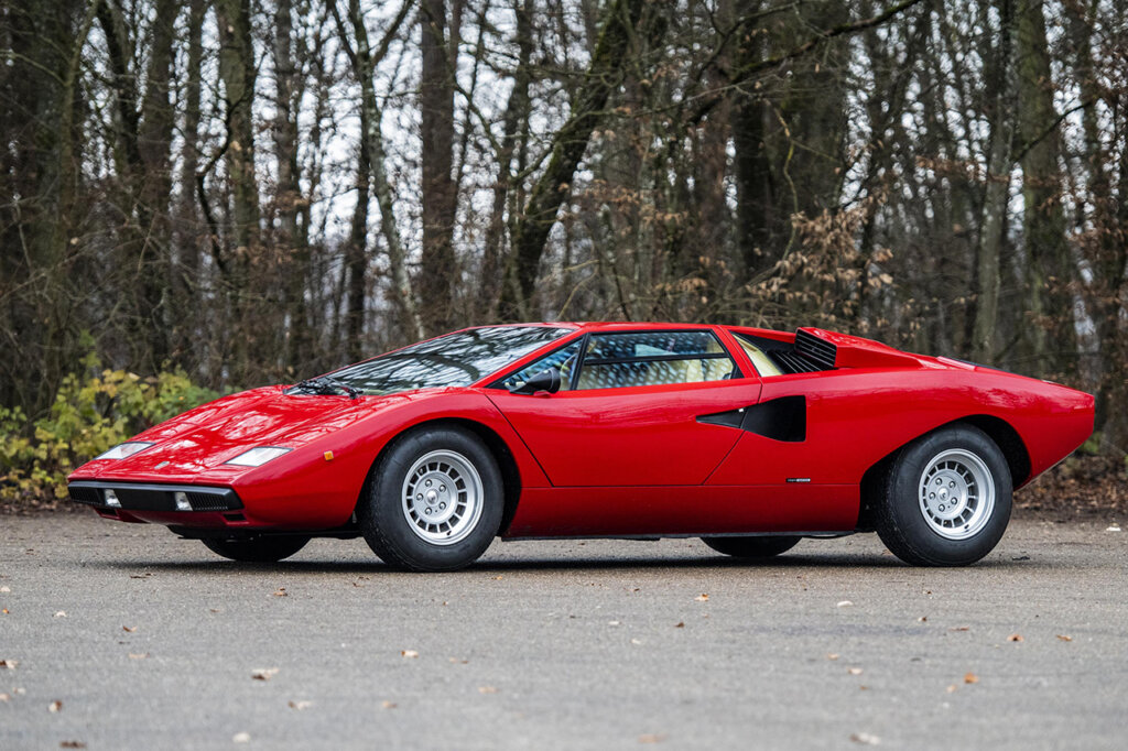 Red LP400 Lamborghini parked with the woods behind it