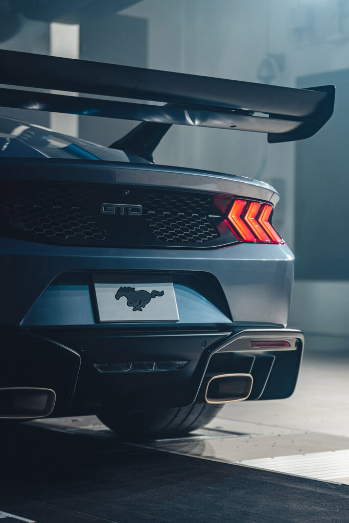 Rear taillights with large spoiler wing of a grey Ford parked on concrete
