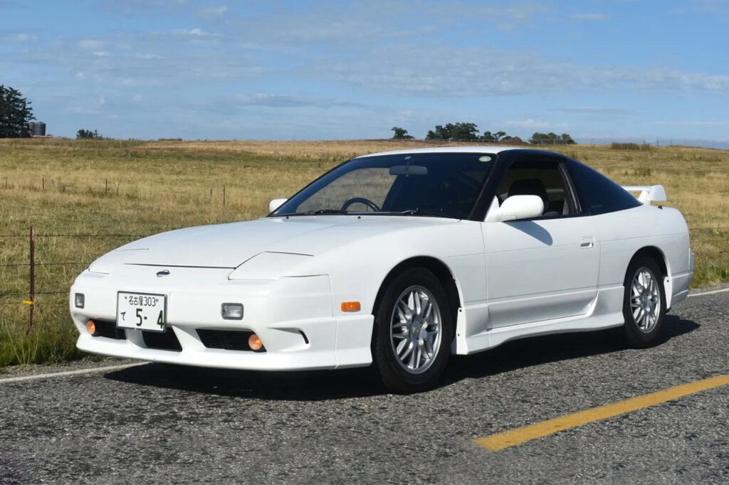 white 180sx on the road in front of a grassy field