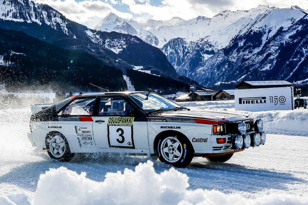 Audi Quattro A2 driving fast on the snow with the icy blue mountains behind it. 