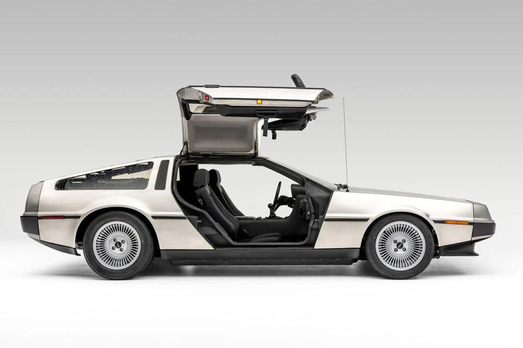 Side profile of a Silver car with gull wing doors open in a white room