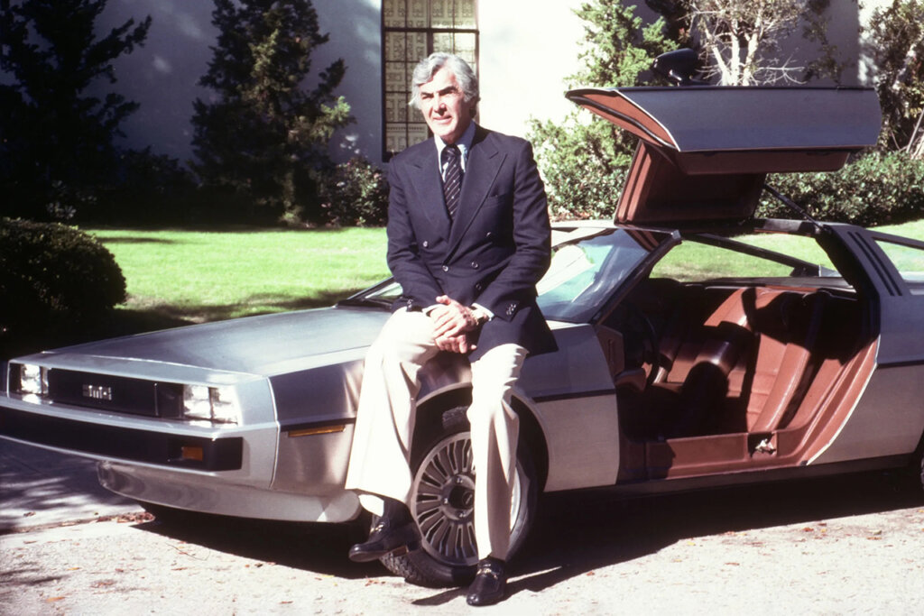 Man in a suit sitting on a DMC12 with the doors open in front of a house