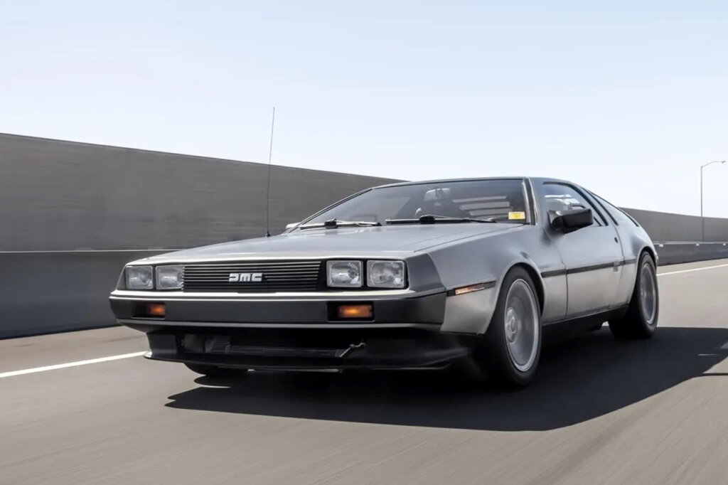 DMC Delorean driving fast on the freeway clear sky behind it and a wall stretching behind