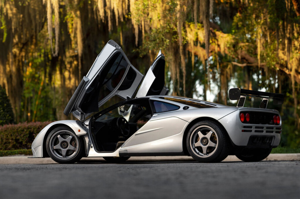 Silver HDK McLaren F1 parked doors open large spoiler wing and sunlight hitting trees