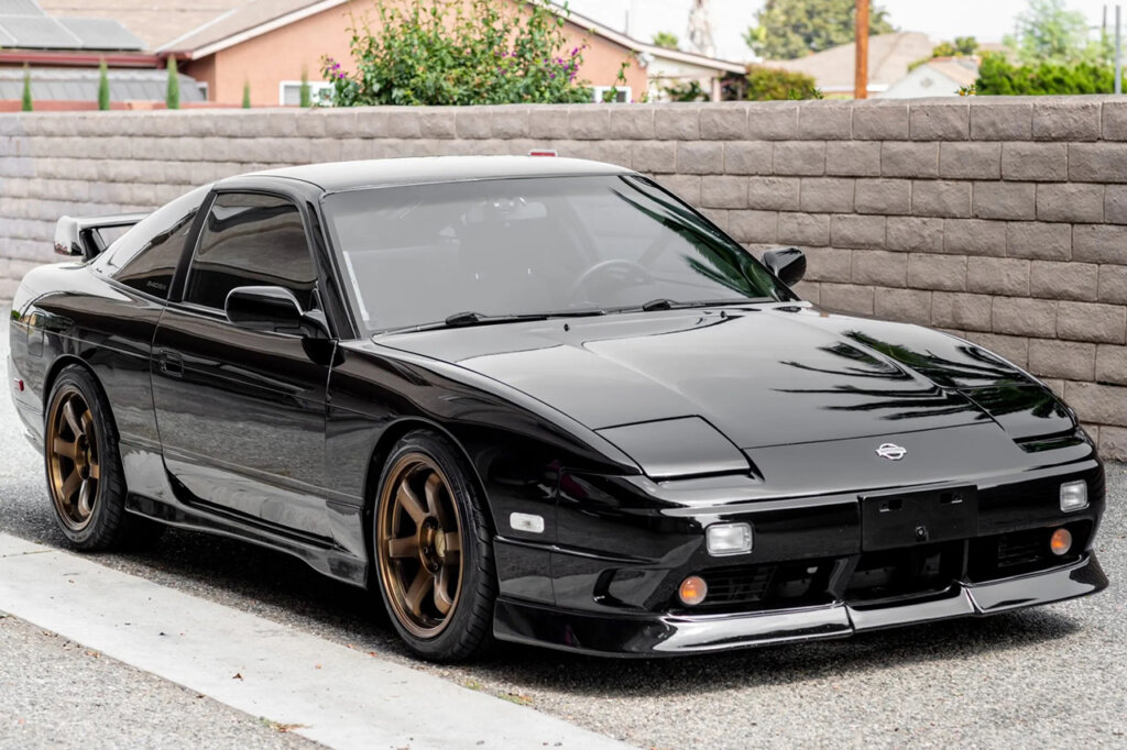 Black Nissan S13 hatch parked in front of a brick wall