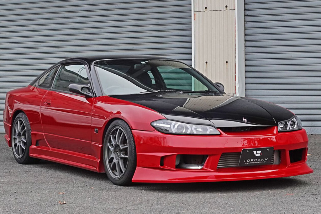 Red Silvia S15 with black painted hood parked in front of two steel garage doors
