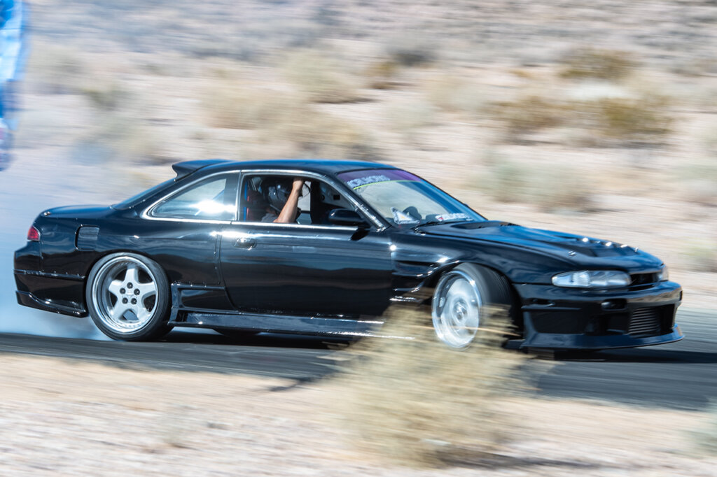 black kouki Nissan drfting with a guy holding onto the interior car handle
