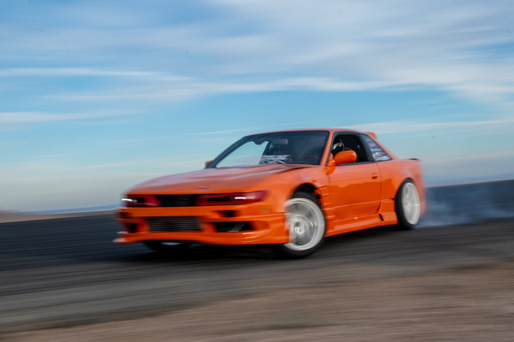 Orange Nissan 240sx S13 drifting in action, blue sky with some clouds in background