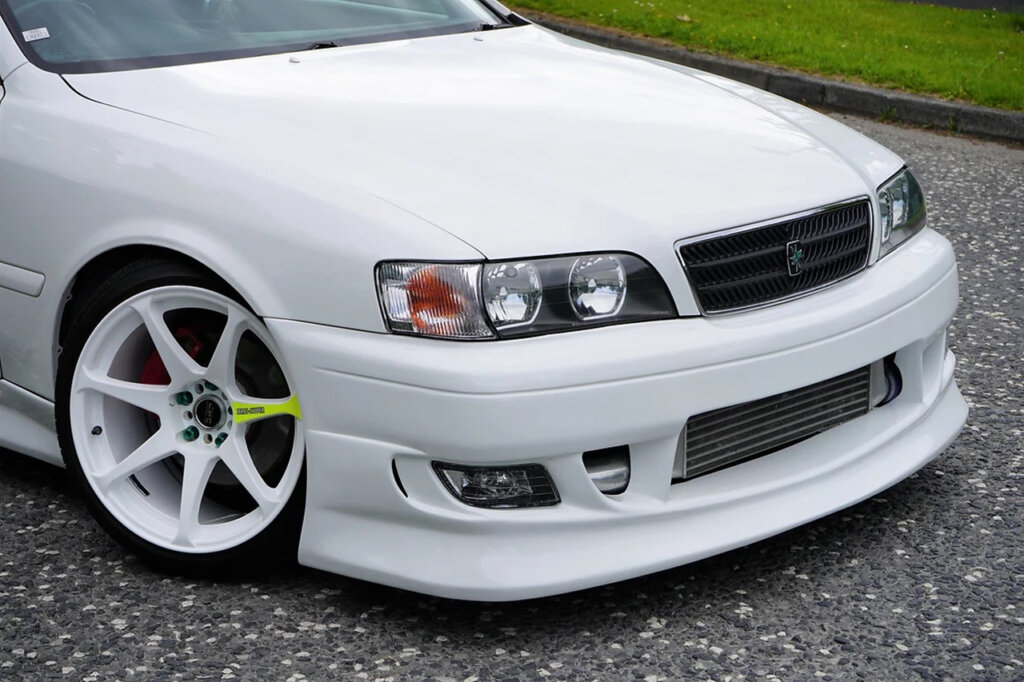 Closeup of a white Toyota Chaser with white wheels that have 1 green stripe on the spoke