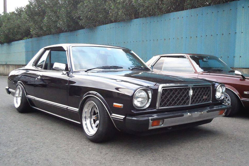 Black Toyota Chaser x30 parked next to a red vehicle and a blue fence behind that