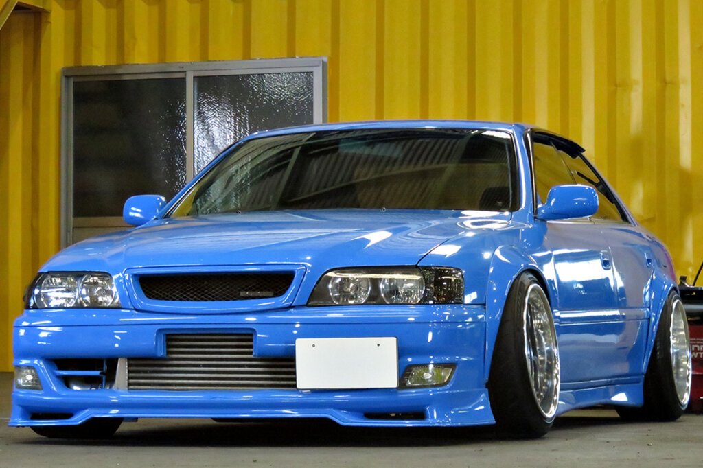 Light blue Toyota Chaser parked in a garage with a yellow wall and window behind the car