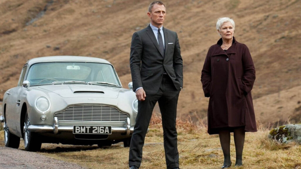 daniel craig and judi dench next to an aston martin db5 in scotland