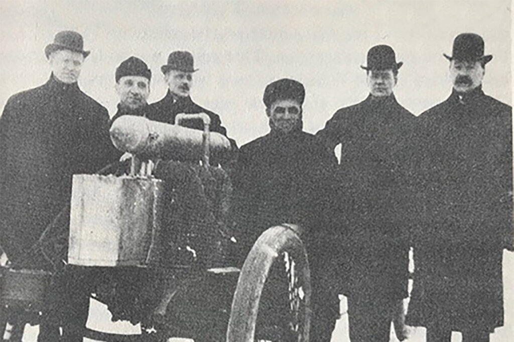 Black and white photo of 6 men standing next to one another with a machine