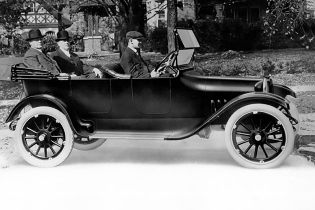 Black and white photo of three men in a car in front of a house
