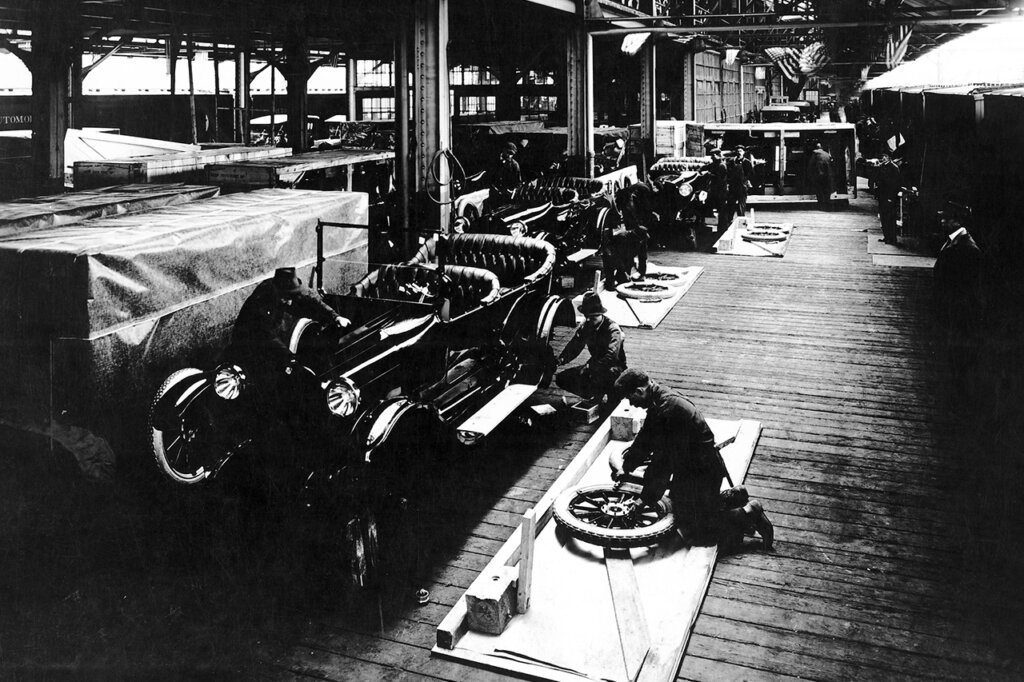 Black and White photo of a man working on a Dodge car part in a car manufacturing warehouse
