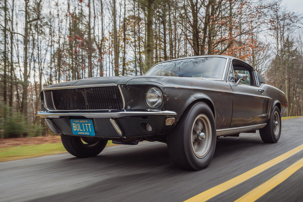 Highland Green Bullitt Ford Mustang driving on a road passing trees