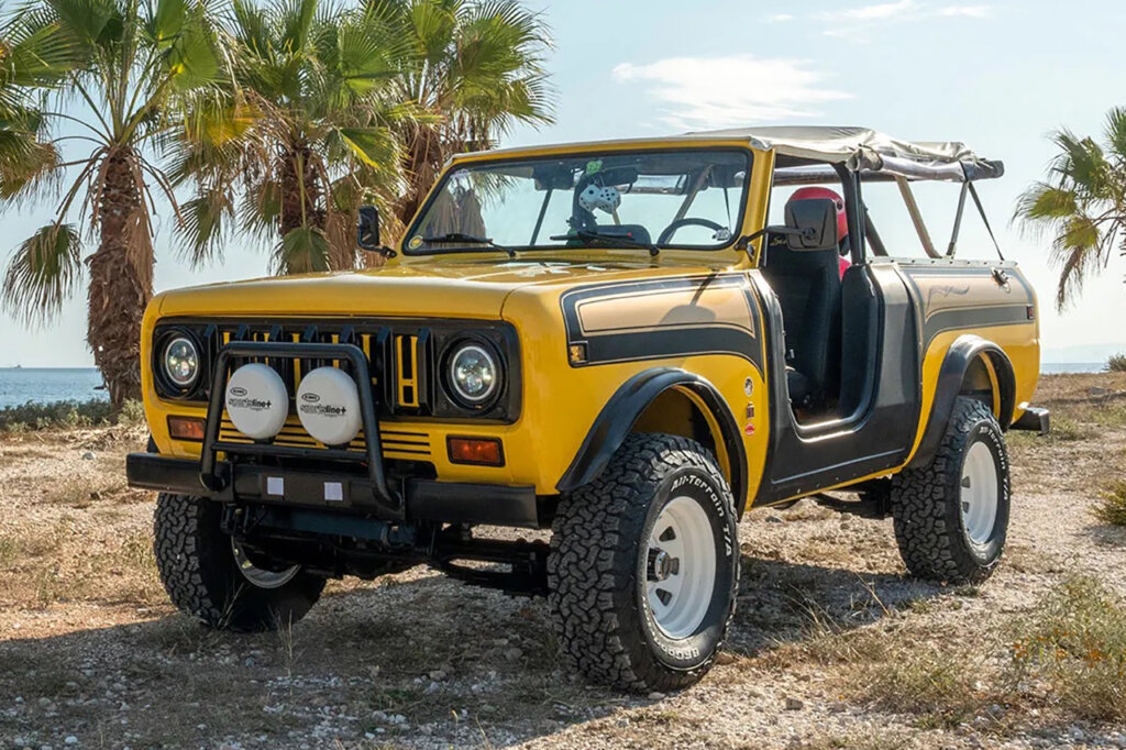 Yellow and black Super Scout II parked on the dirt with palm trees in the background