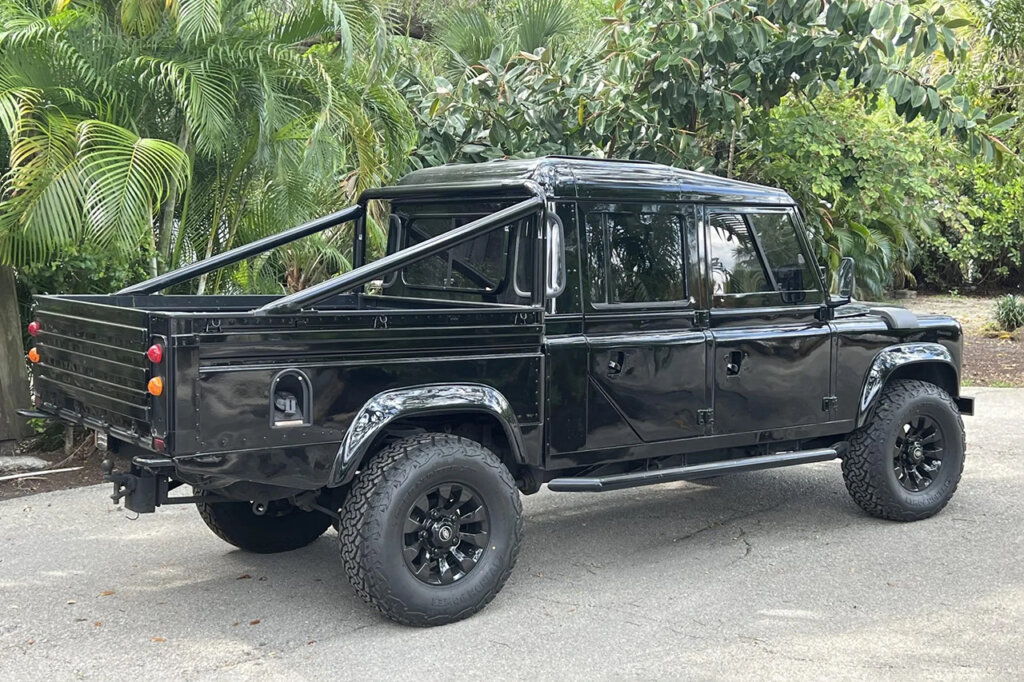 Black Land Rover 127 parked in a driveway next to trees