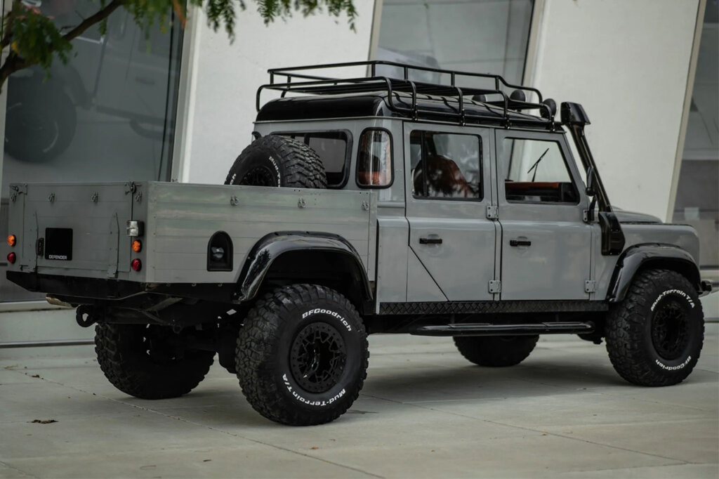 Grey Land Rover 130 next to a building with glass windows