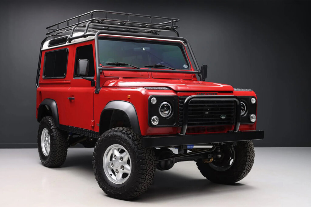 Red Land Rover 90 sitting in a room with a dark background and white floor
