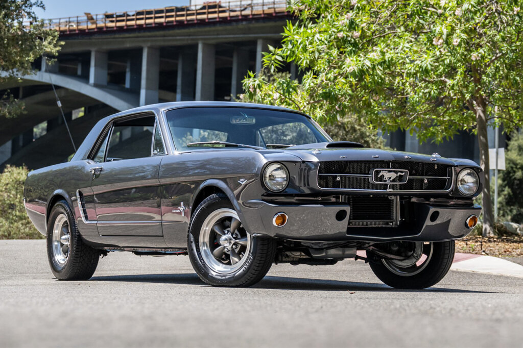 Grey custom Ford Mustang parked with a bridge in the background
