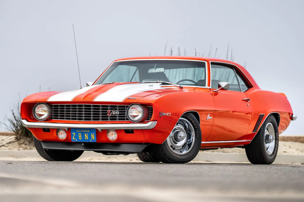 Orange with white racing stripe Chevrolet Camaro parked on a parking garage with a grey sky behind it
