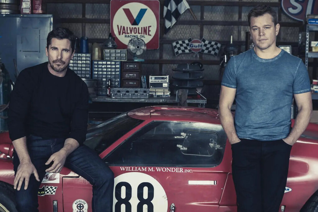 Two men leaning on a red Ford GT with some racing items behind it