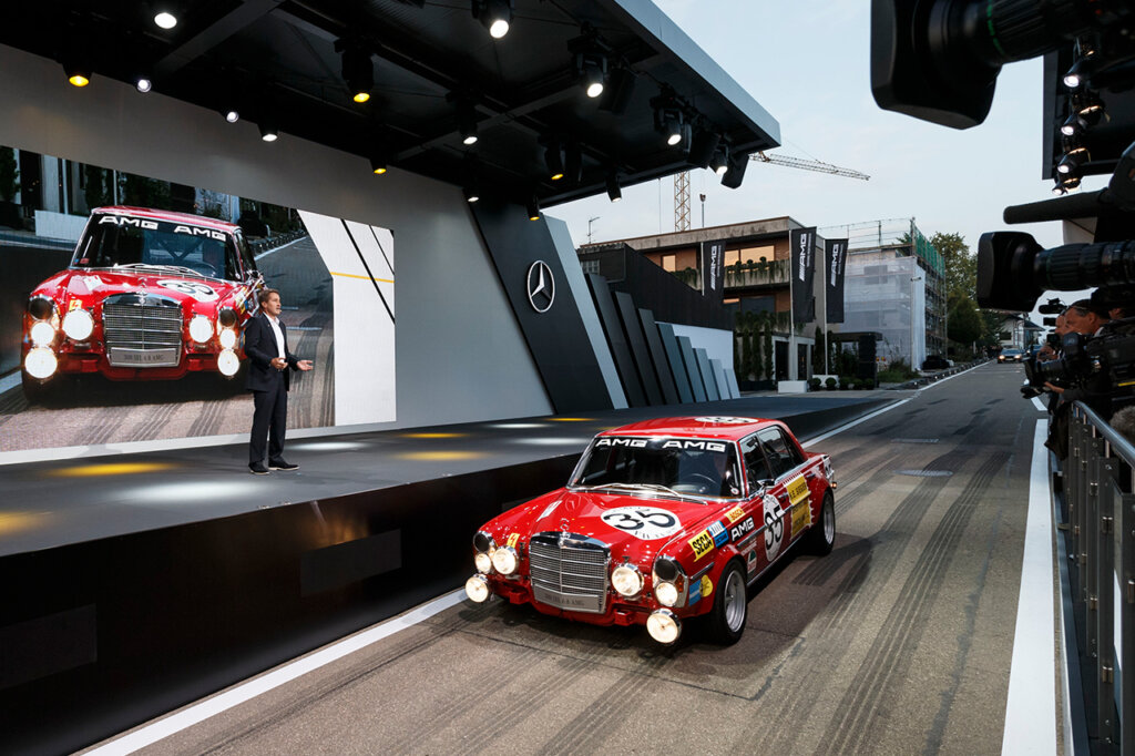 replica Red Pig 300SEL parked on a road with a man in a suit on a stage