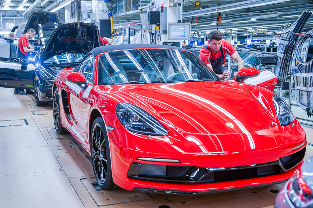 Red vehicle being worked on on an assembly line by a man in uniform