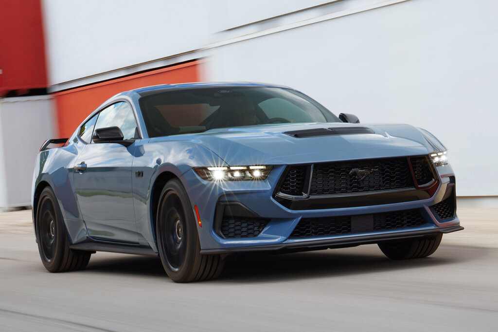 Blue Mustang GT with headlights on driving fast on asphalt