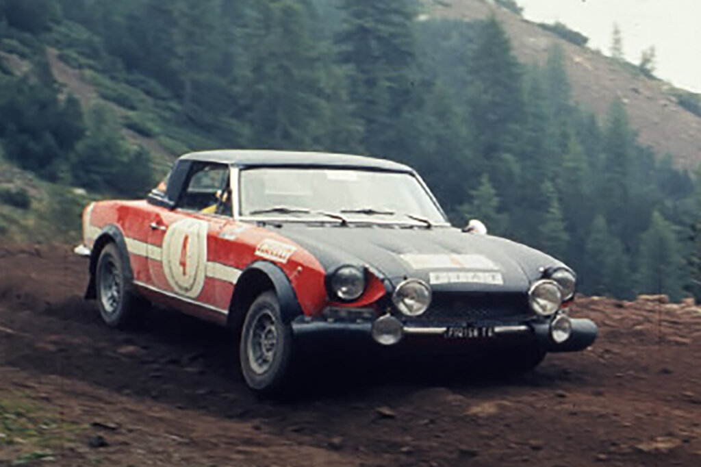 Red and black Fiat 124 rally car on a dirt road