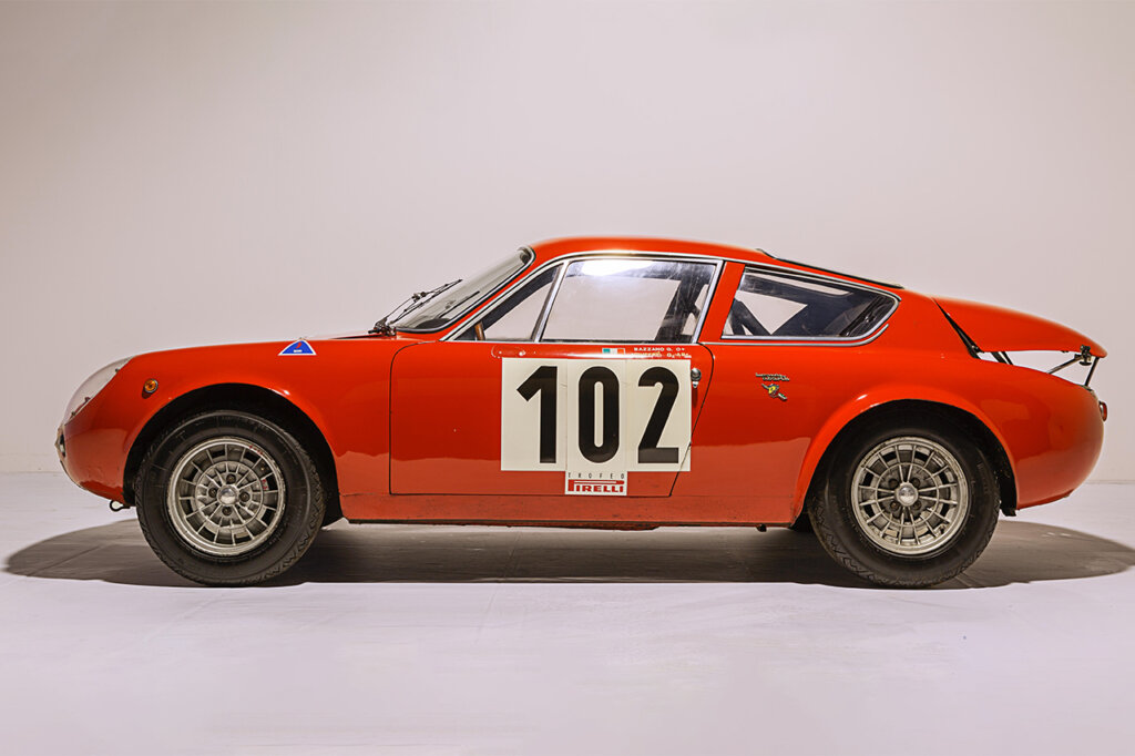 Red Abarth Simca 1300 side profile with 102 on the door and against a white background